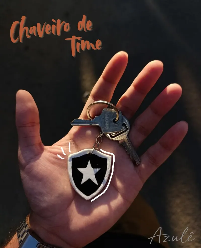 Mão segurando um chaveiro com chave e um escudo preto e branco de cerâmica fria