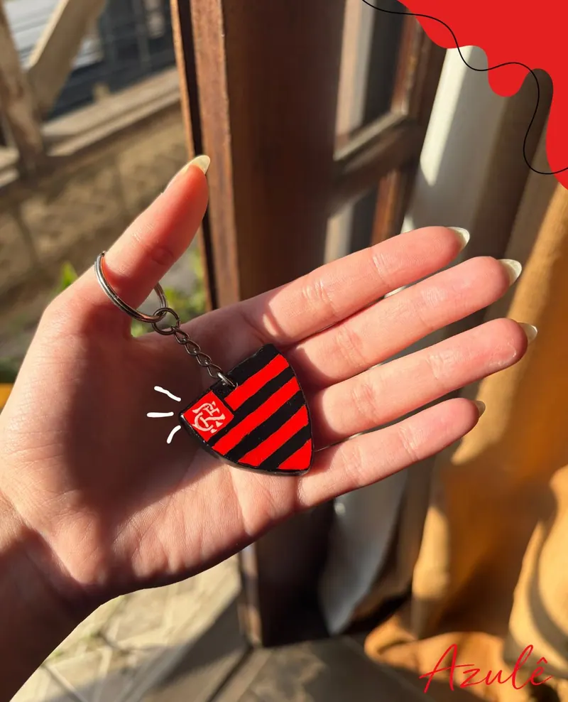 Mão segurando um chaveiro de cerâmica fria com o escudo de um time de futebol